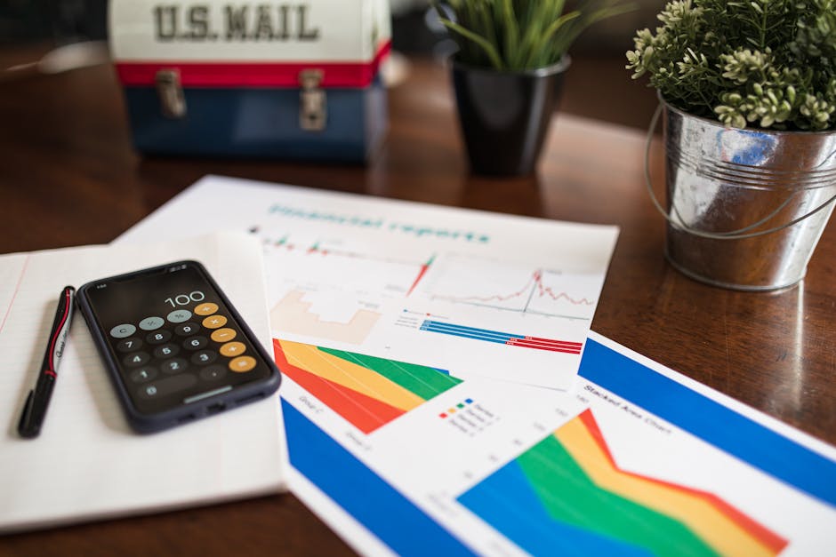 A workspace with financial charts, smartphone calculator app, pen, and plant on a wooden desk.